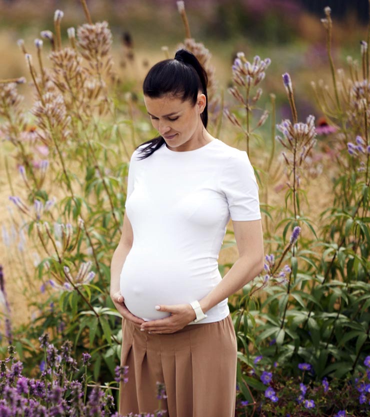 Pregnant women standing in a flower field holding her belly. | Fertility Cleanse Detox